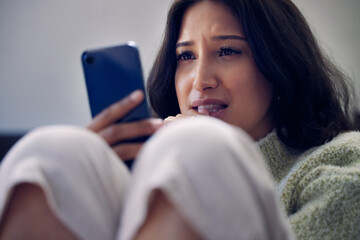 Woman, phone and depression or anxiety for cyberbullying, social media and internet in house. Girl, smartphone and sad or mental health as victim for online, harassment and virtual gossip or rumor
