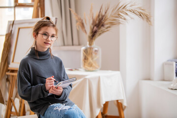 A girl draws with a pen in a notebook in an art light studio