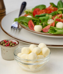 Mozzarella balls in glass bowl and salad on a white background