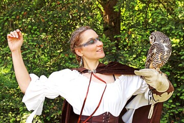 Eine Frau, als mittelalterliche Jägerin verkleidet, hat einen Waldkauz auf ihrer Hand