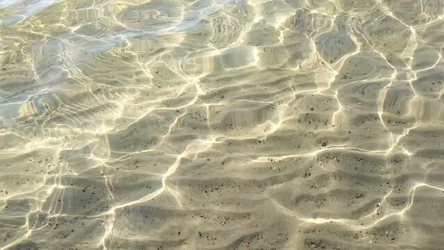 Sand ripples on the sea bottom. Beautiful light caustics effect on shallow beach water, sunny light effect in slow motion for video projects. Relaxing vacation holiday video