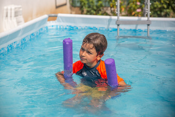 Smiling boy with purple swim noodle in an outdoor pool, ready for summer fun