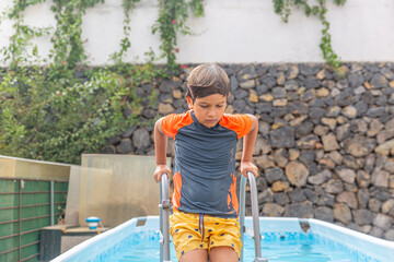 Expressive young boy emerging from a refreshing pool climb, animated posture against a residential...