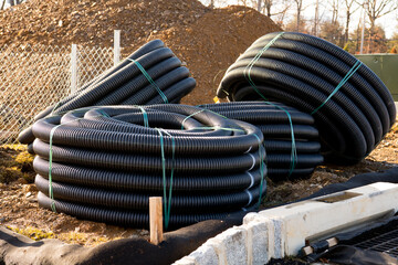 many rolled coils of new black corrugated plastic electric plumbing drainage pipe prepared for...