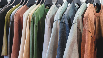 A row of shirts hanging on a rack, with some being green and others being brown. The shirts are all...