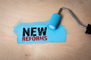 NEW REFORMS. Blue paint and paint roller on a plywood background