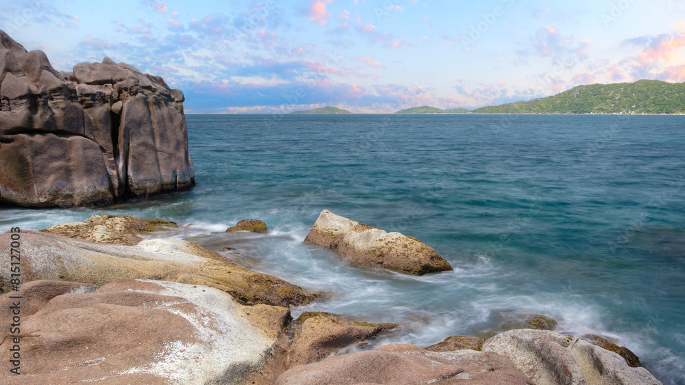 Poster a rocky shoreline with a calm ocean in the background. the water is a deep blue color and the sky is