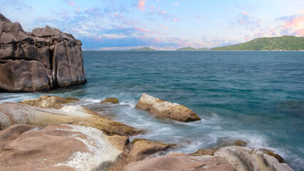 Naklejka premium A rocky shoreline with a calm ocean in the background. The water is a deep blue color and the sky is a light blue color