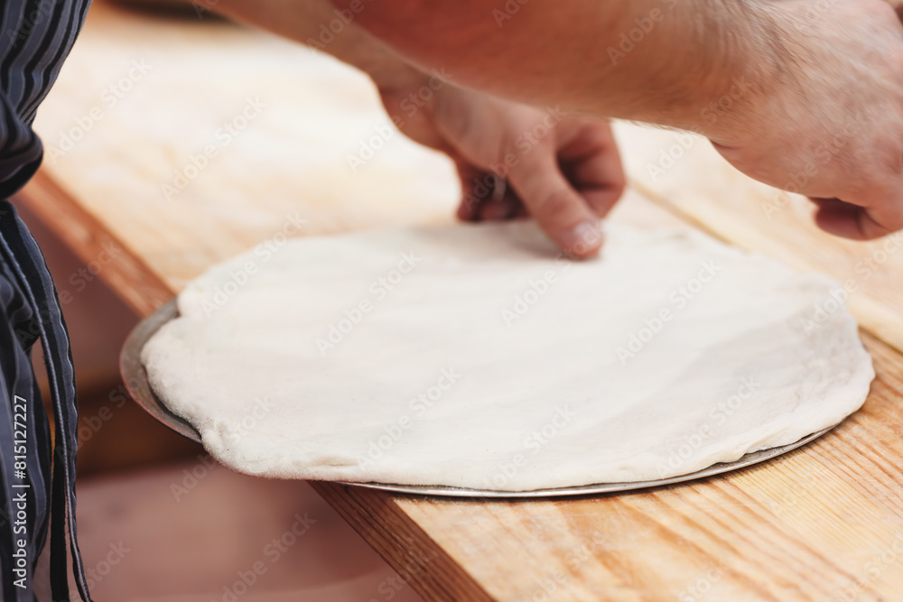 Poster a person is making a pizza dough on a wooden table. the dough is spread out on a pan and the person 