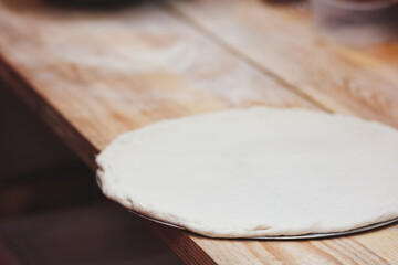 A pizza dough is sitting on a wooden table. The dough is white and has a circular shape