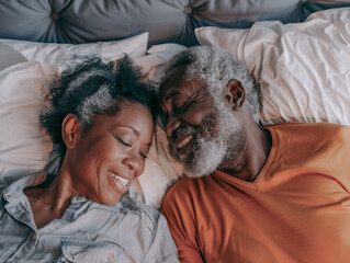 Elderly black couple lying in bed together, smiling as they sleep.