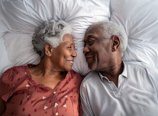 Elderly black couple lying in bed together, smiling at each other.