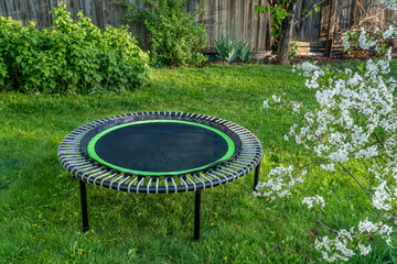 mini trampoline for fitness exercising and rebounding in a backyard, spring scenery with cherry tree in blossom