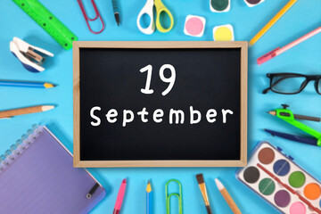 September 19 written in chalk on black board. Calendar date 19th of September on chalkboard on blue blurred school stationery background. Back to school. School event schedule date. Month of autumn.