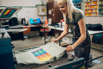 Smiling print shop worker putting screen printed shirt in drying machine