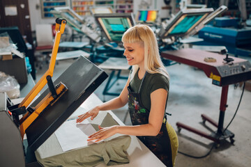 Smiling printing workshop worker using heating press and transfer on tee