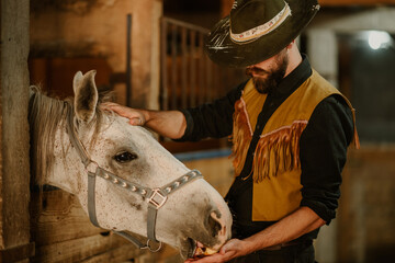 Young attractive farmer is feeding a horse in horse stall at ranch.