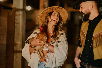 Happy rancher couple standing at animal farm with chicken in hands.