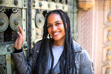 A happy young black female with afro braids is sitting on the steps near a big antique doors