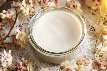Homemade horse chestnut cream in a glass jar on a table with freh Aesculus hippocastanum flowers