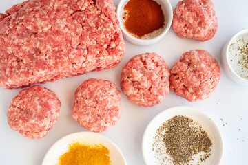 Ground beef, shaped patties and spices on white background. Barbecue preparations.