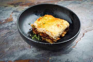 Traditional Greek moussaka with beef mince, eggplant and bechamel sauce served as close-up in a Nordic design Bowl on a stone board