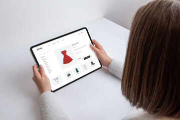 Woman holds tablet with an e-commerce webpage, searching for a red dress. Modern shopping at her...