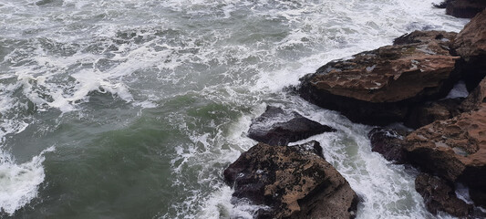 The waves of the sea are crashing against the rocks on a stormy day, creating a dramatic and powerful scene.