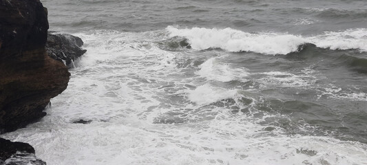 The waves of the sea are crashing against the rocks on a stormy day, creating a dramatic and powerful scene.