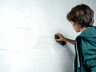 A boy is spraying a wall with a can of spray paint