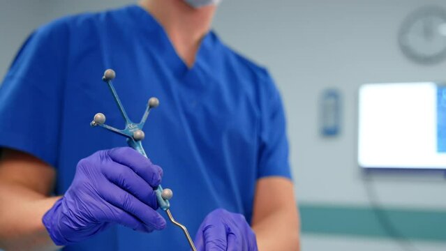 Unrecognized doctor in blue uniform holding a navigated tool equipped with reference frame for neurosurgical operation. Medic attaches the instrument to the head of the patient. Close up.