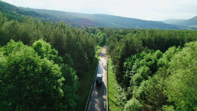 Aerial drone camera follows a grey off road overlanding van with solar panels on the roof driving in lush green forest road after rain. Overland and vanlife camper travel lifestyle