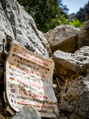 Demolished warning sign at Torrent de Pareis canyon, emphasizing the challenging terrain and importance of safety measures for this area, with instructions in Spanish, Catalan, German, English, French