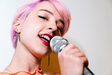 A woman singing into a microphone with pink hair. young woman sings enthusiastically and playfully