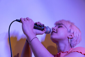 A woman singing into a microphone with pink hair. young woman sings enthusiastically and playfully