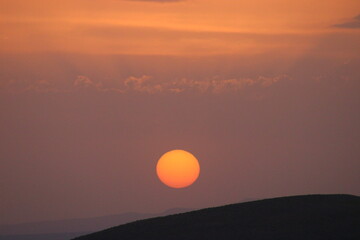 a sunset with clouds and a orange sun setting in the sky.