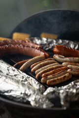 Cooking hot dogs and sausages on the grill with fish in foil.