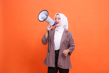 Young Asian woman in hijab shouting holding megaphone isolated on orange background, Speech,...