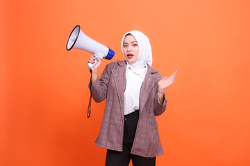 Young indonesia woman in hijab shocked facing front holding megaphone speaker palm to side isolated...