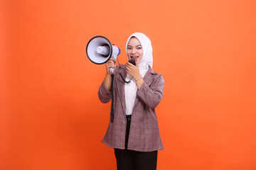 Cheerful young Asian woman in hijab facing front shouting using mic holding megaphone speaker...