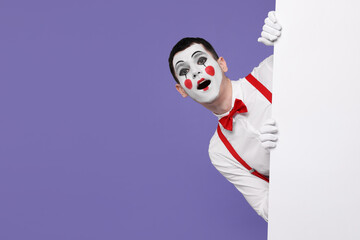 Funny mime artist peeking out of blank poster on purple background. Space for text