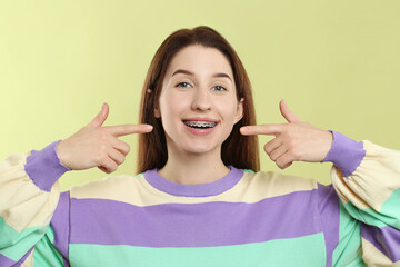 Portrait of smiling woman pointing at her dental braces on light green background