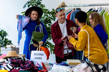 Man shopping vintage clothes in second hand store with girl friends. Used shirts, jackets, bags get...