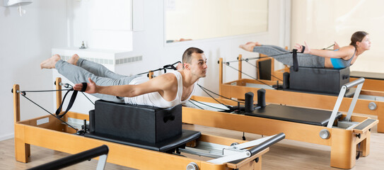 Man doing pilates exercises with reformer bed in studio. Active lifestyle and fitness concept.