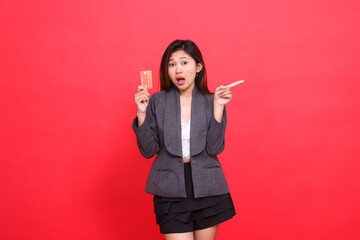 Asian office girl expression shocked, holding a debit credit card while pointing to the left,...