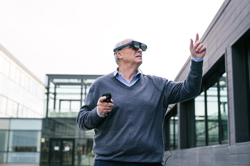 A senior executive in a sweater interacting with virtual reality glasses while standing outside a...