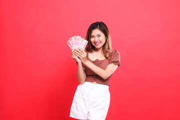 Cheerful indonesia woman's expression holding rupiah currency in both hands, wearing a brown blouse...