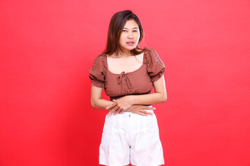Asian woman's expression in pain, her stomach hurts, wearing a brown blouse and shorts with a red...