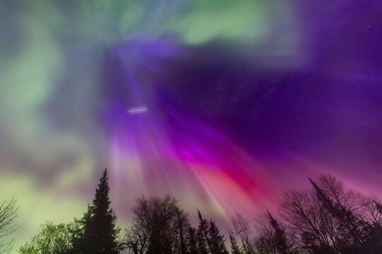 Northern lights erupt over Minnesota in a dark sky overhead shining rainbow of Aurora light as a satellite passes above leaving a trail of white light