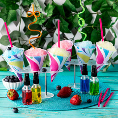 Fruit flavoured shaved ice snow cones with flavour syrups in front.